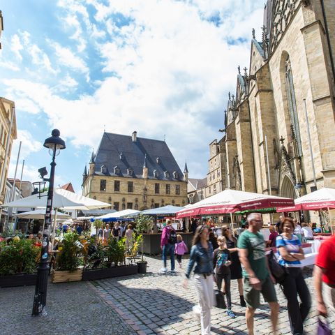 Lebhafter Marktplatz in Osnabrück mit historischen Gebäuden und Cafés, wo Einheimische und Besucher das lebendige Stadtleben genießen.